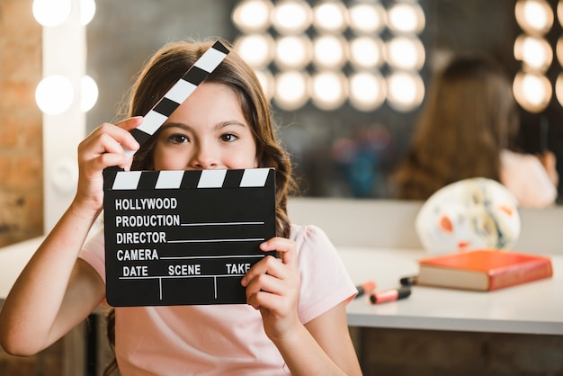 Free photo girl holding clapperboard in front of her mouth