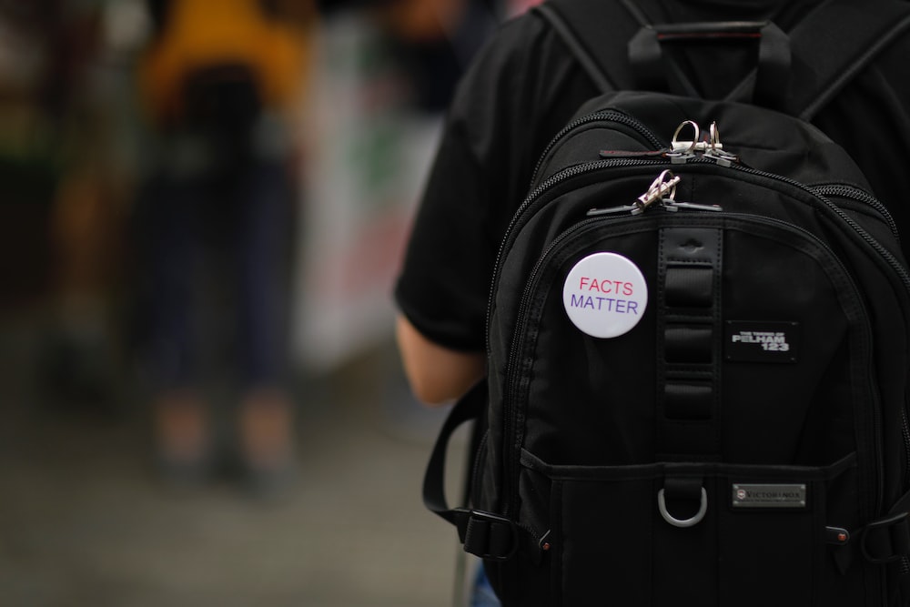 A whiteâ€œFacts matterâ€ pin on a black backpack on a person's back